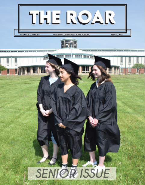 Three young women stand in caps and gowns in front of the WCHS library on the main lawn