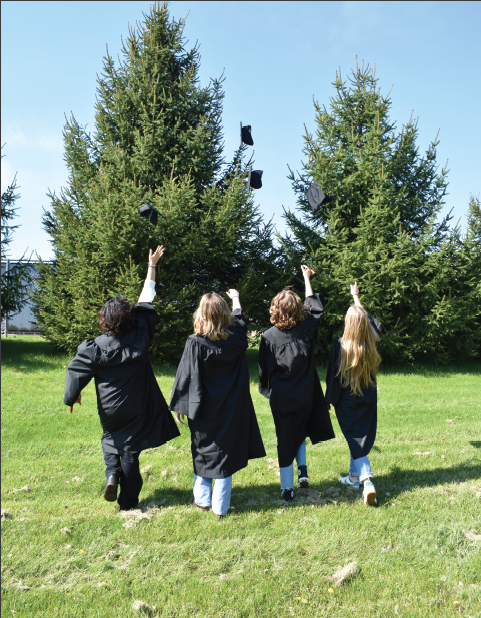 four seniors walk away from the camera and toss their hats into the air