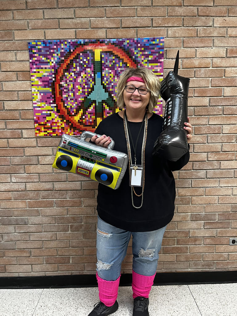 Teacher in 80s clothing holding giant blow up phone and boom box